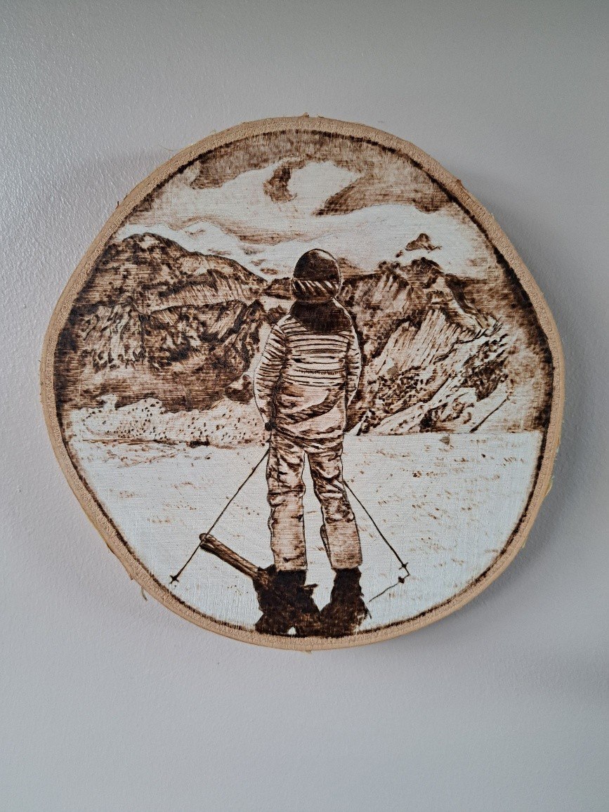 Skier facing mountain range burned onto birch wood slice